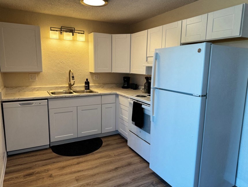 A white refrigerator stands in a kitchen with white cabinets and a black mat on the floor.