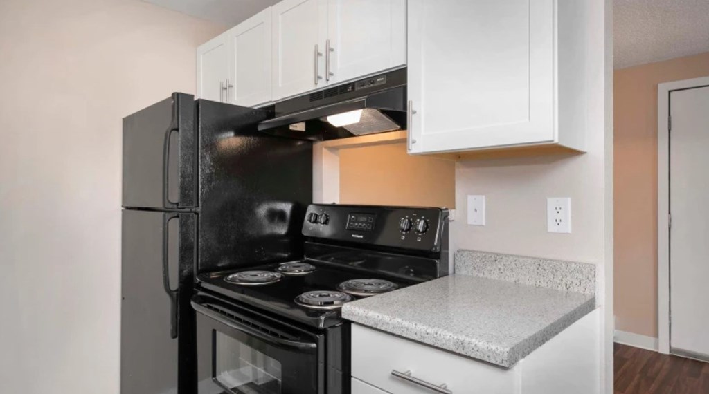 A black refrigerator is in a kitchen with white cabinets.