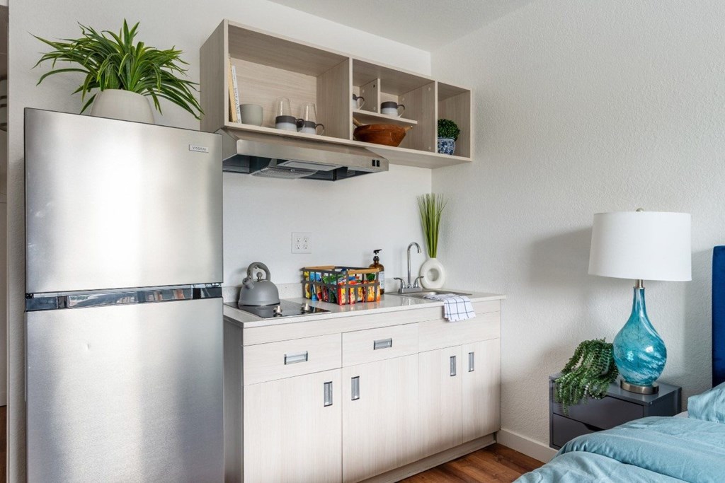 A kitchen with a refrigerator, a counter, and a bed.