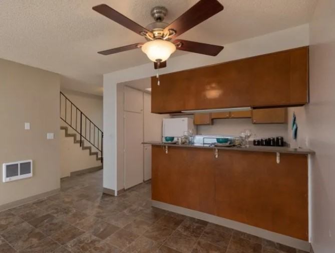 A room with a ceiling fan and a counter with a staircase in the background.