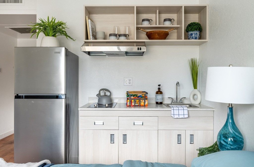 A kitchen with a refrigerator, a counter, and a shelf with various items.