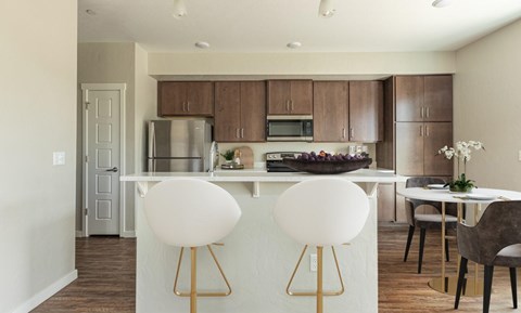 A kitchen with a white island and brown chairs.