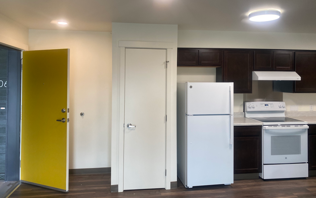 an empty kitchen with white appliances and a yellow door