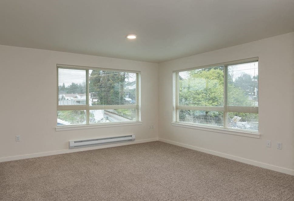 an empty living room with two windows and carpet