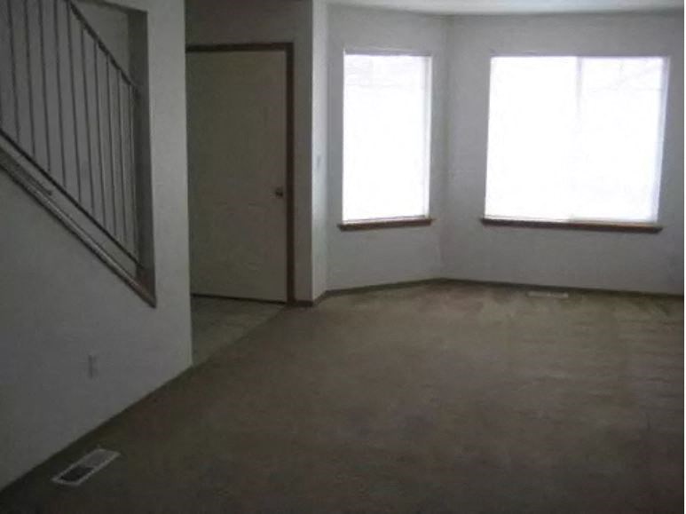 an empty living room with three windows and a door