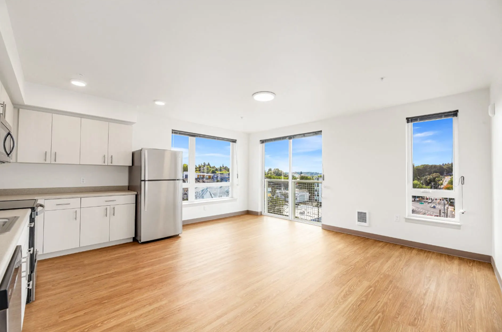 an empty living room with a kitchen and a large window