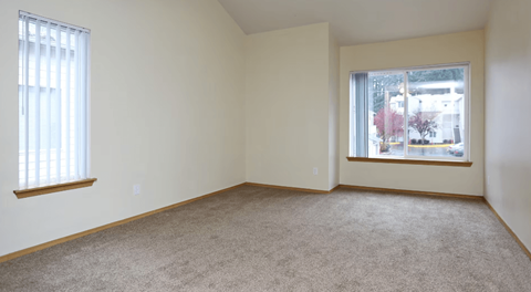 A room with a carpeted floor and two windows.