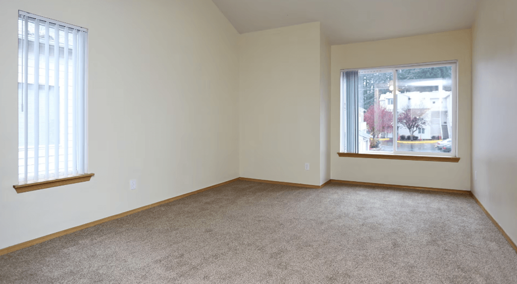 A room with a carpeted floor and two windows.