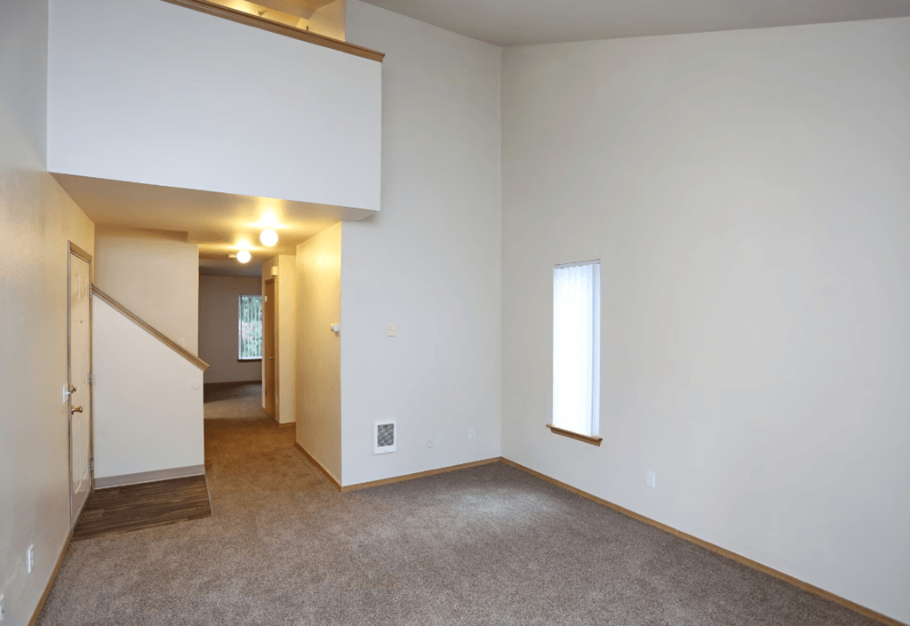 A large empty room with a carpeted floor and a window.