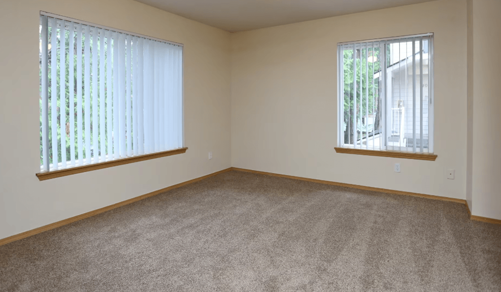 A room with a carpeted floor and two windows.