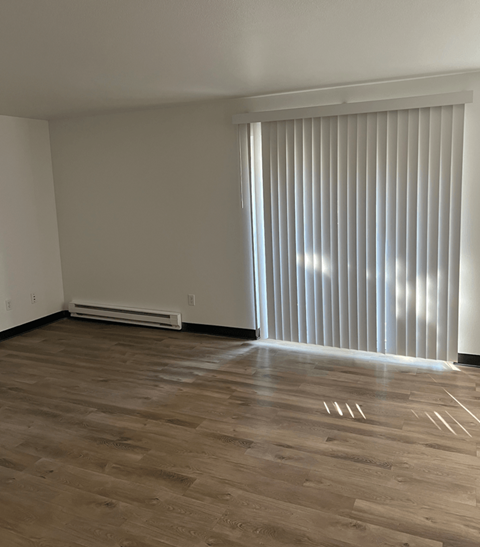 a living room with wood floors and a large window with white blinds