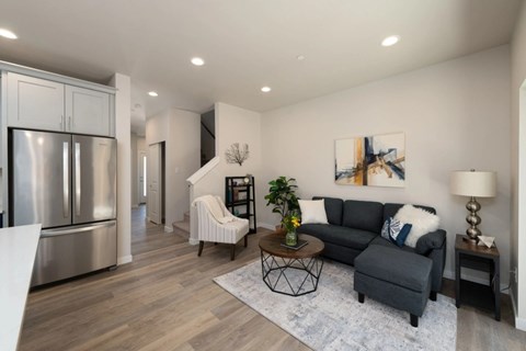 A modern kitchen with a refrigerator, a dining table with chairs, a couch, and a painting on the wall.