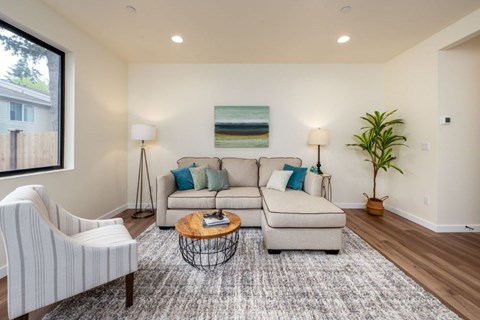 A living room with a white sofa, a white chair, a coffee table, and a plant.