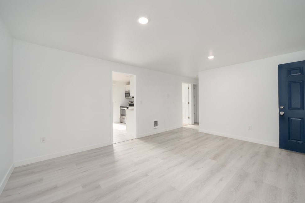 A spacious room with a dark blue door and light wooden flooring.