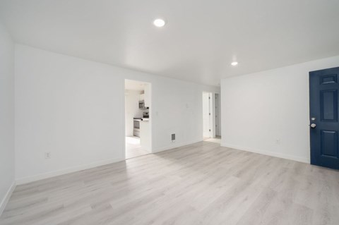 A spacious room with a dark blue door and light wooden flooring.