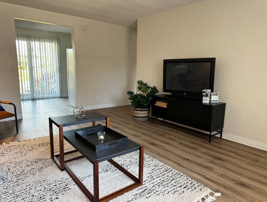 A black coffee table with a candle on it sits in the middle of a room with a flat screen TV mounted on the wall.