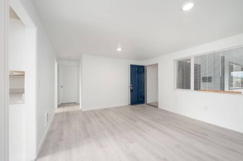 A spacious room with a wooden floor and a large window with blinds.