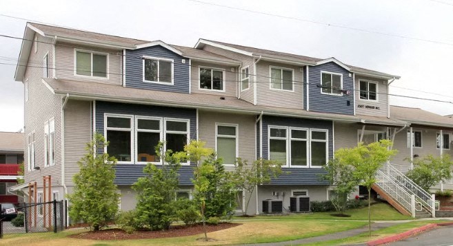 A grey and blue two story apartment building with a red fire hydrant in front.