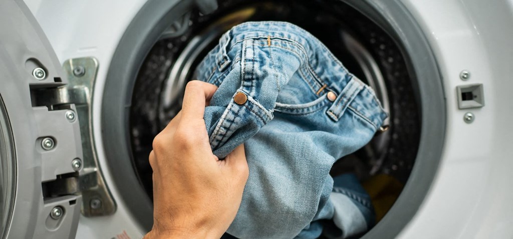 a person putting a pair of jeans into a washing machine