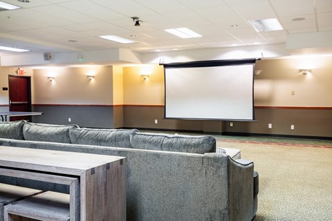 A conference room with a white screen and grey couches.