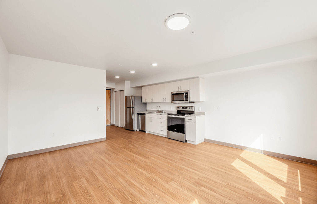 the living room and kitchen of an apartment with wood floors and white walls