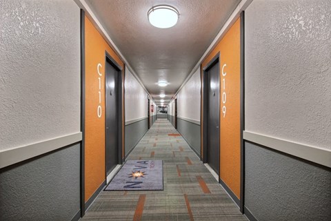 a long hallway with orange doors and a rug in the middle
