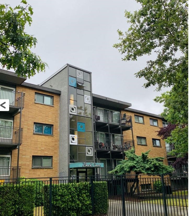 A modern apartment building with balconies and a black fence in front.