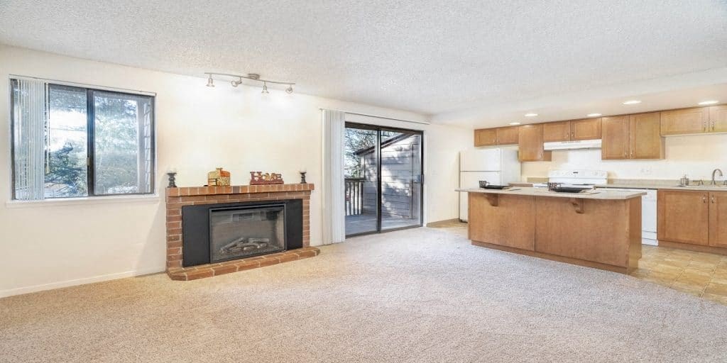 an empty living room with a fireplace and a kitchen