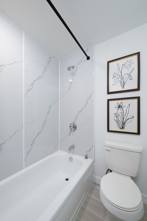 A white toilet sits next to a white bathtub in a bathroom with marble walls.