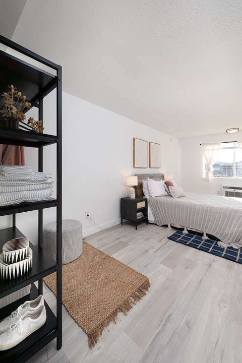 A bedroom with a bed, nightstand, and a shelf with various items.