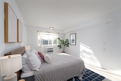 A bedroom with a bed, nightstand, lamp, and window.