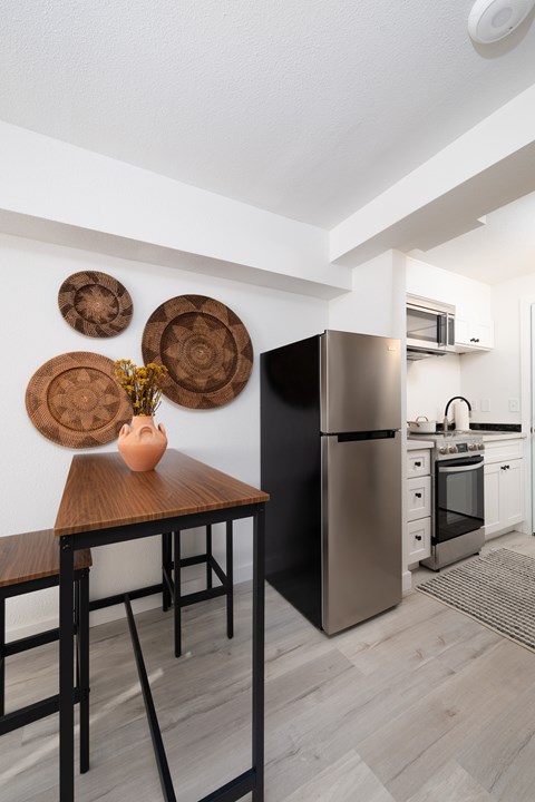 A kitchen with a black fridge and a wooden table with a vase on it.