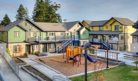 A playground with a yellow slide and a green play structure in front of a row of houses.