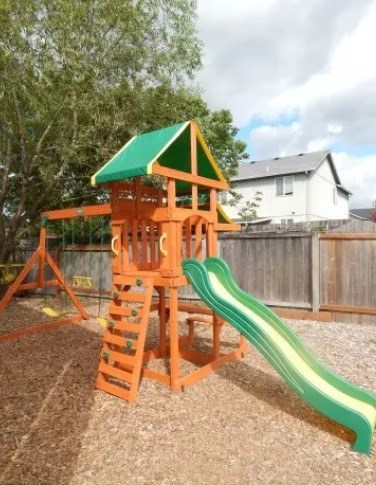 A wooden playground structure with a green roof and a green slide.