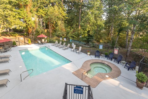 A pool with a hot tub and chairs in a wooded area.