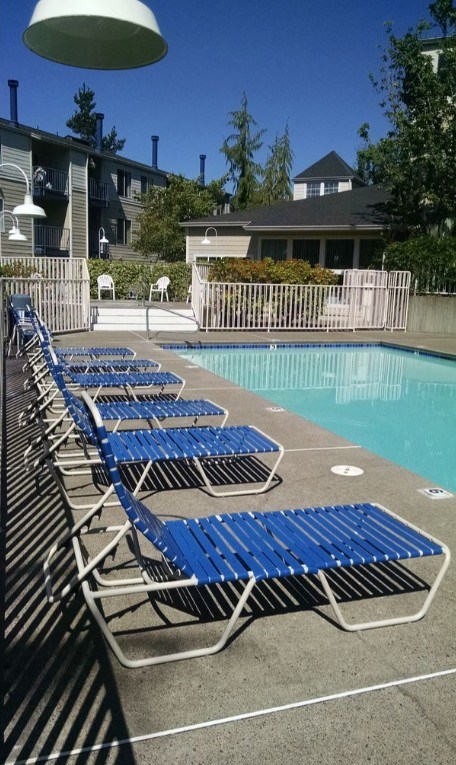A poolside with blue chairs and a white umbrella.