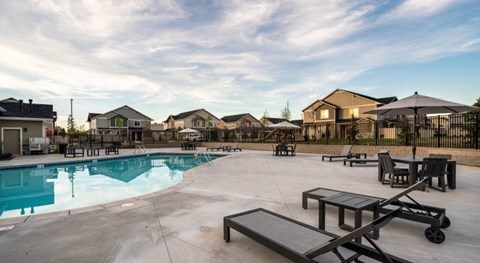 a swimming pool with benches and umbrellas in front of houses