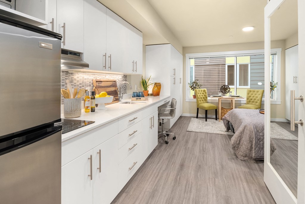 a kitchen with white cabinets and a living room with a bed