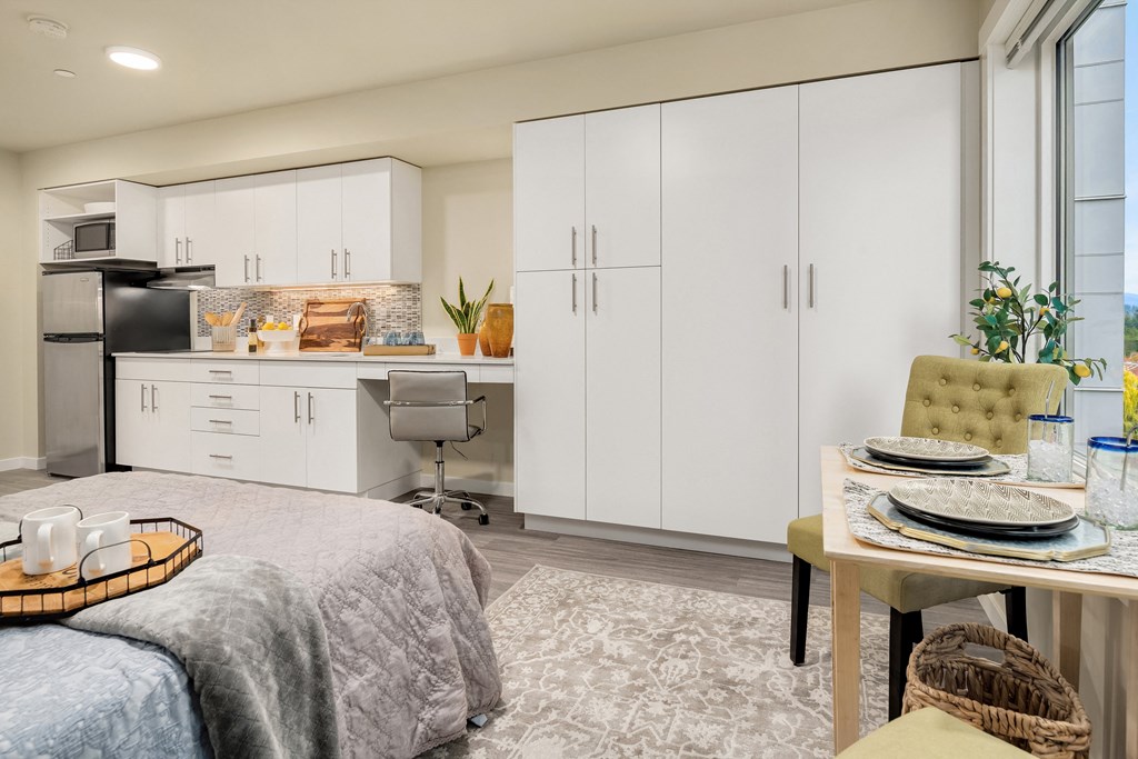 a bedroom with a bed and a desk and a kitchen