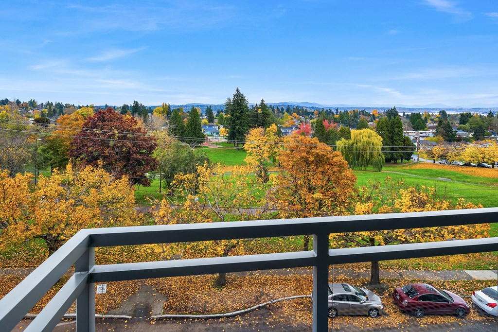 the view from the top of a balcony overlooking a park with trees and cars