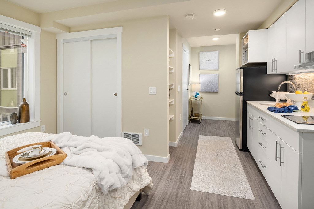a bedroom with a bed and a kitchen with white cabinets