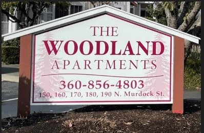a sign for the woodland apartments on the side of the road