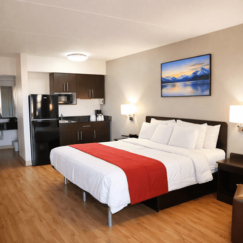 A bedroom with a large bed and a fridge in the corner.