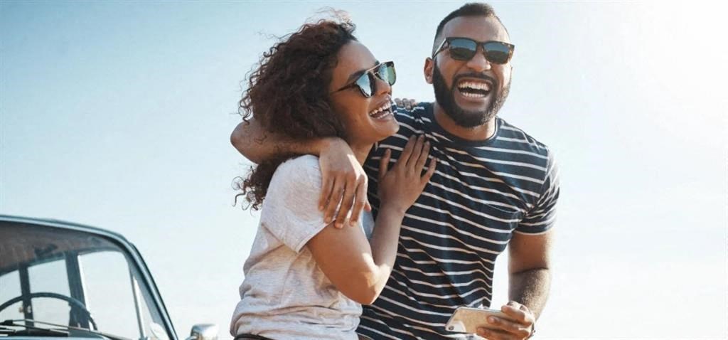 a man and woman laughing in front of a car