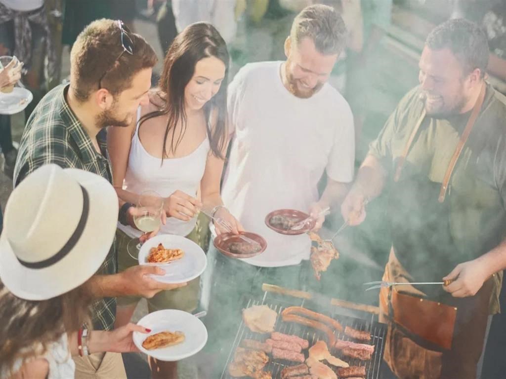 a group of people standing around a grill cooking food on plates