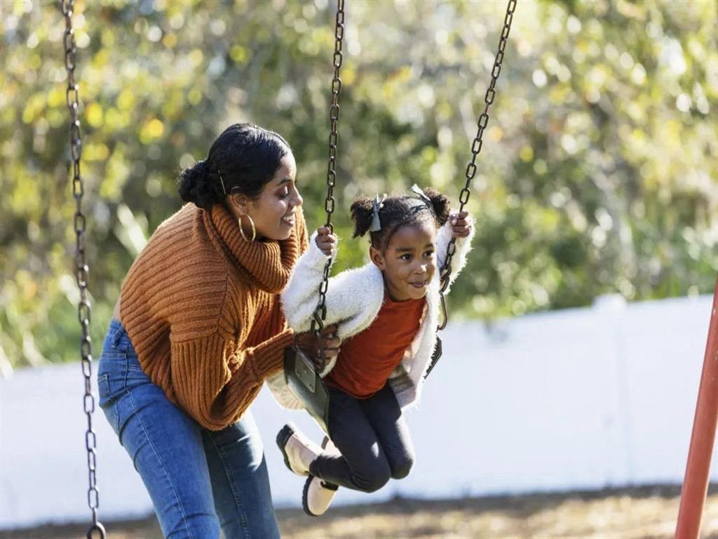 a woman pushing a child on a swing