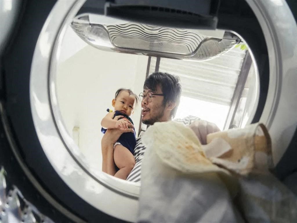a man holding a baby looking at his reflection in a washing machine