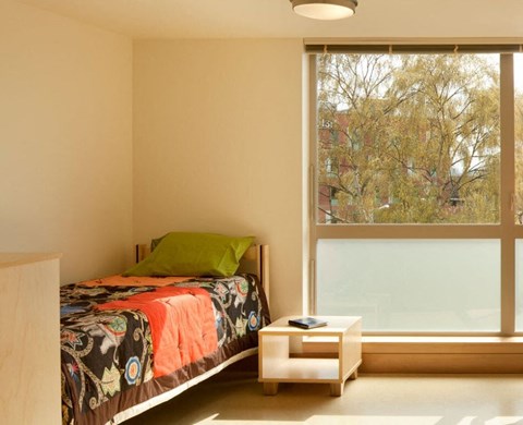 A bedroom with a bed, nightstand, and window overlooking a tree-filled area.
