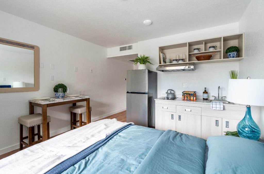 A bedroom with a bed, a table, and a refrigerator.