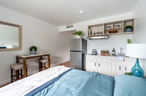 A bedroom with a bed, a table, and a refrigerator.